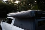 Rigdup 270 degree awning packed in its cover, mounted on the roof rack of a white 4WD ute